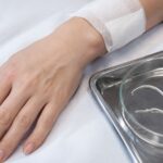 Medical setup showing a bandaged hand of a woman after surgery and a petri dish with parasite worms in human body.